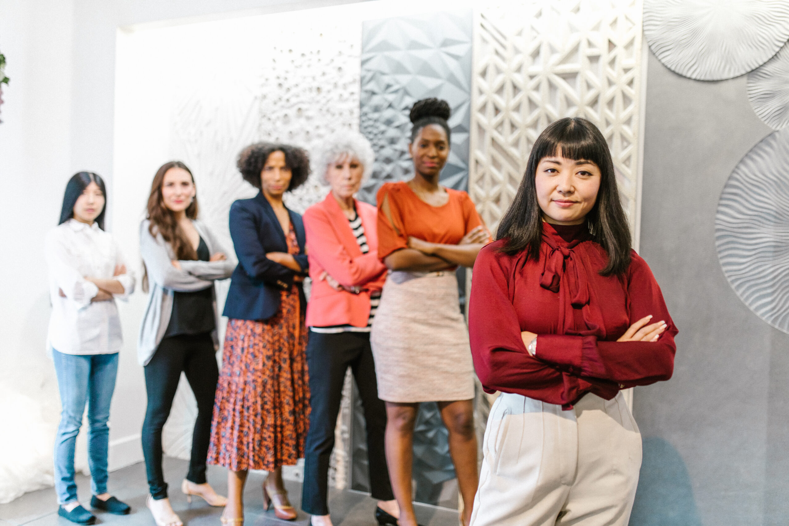 A woman in red long sleeves standing with her arms crossed with people standing behind her