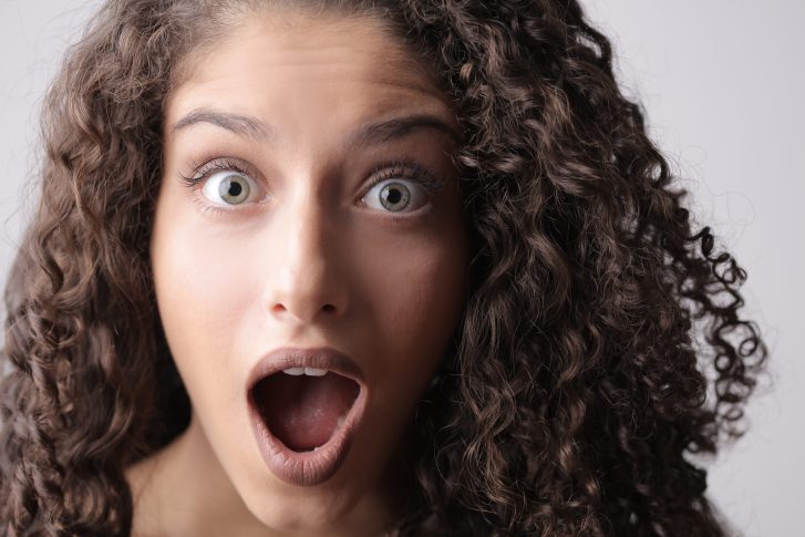 Close up photo of shocked woman with brown curly hair