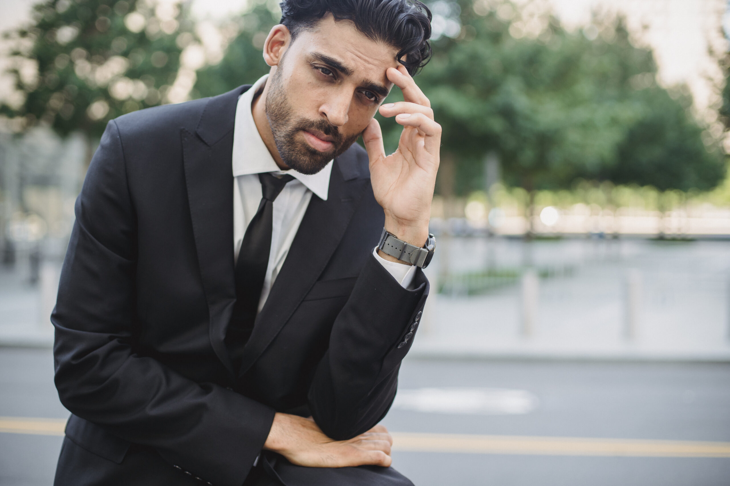 Photo of a man in a black suit with his hand on his head